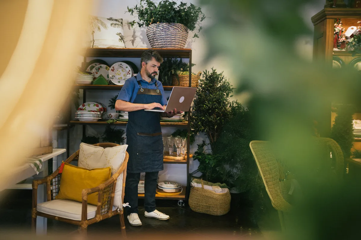 E-commerce store owner reviewing Google Ads sales and ROAS data on a laptop beside packed product inventory