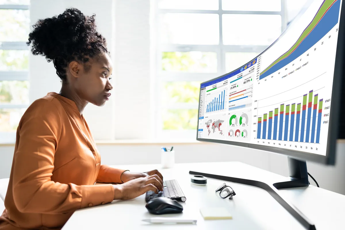 A marketing analyst reviewing channel spend, leads, and revenue charts on a widescreen dashboard at a desk
