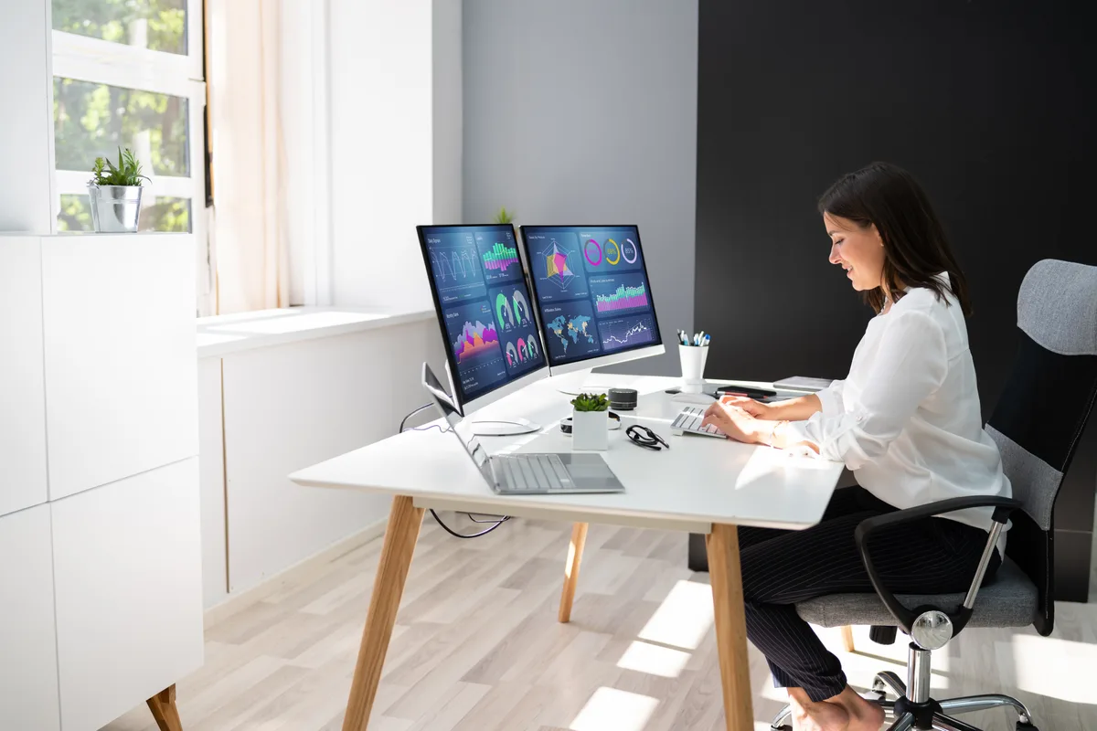 Marketing analyst comparing landing-page conversion reports on two monitors to find which SEO pages produce customers