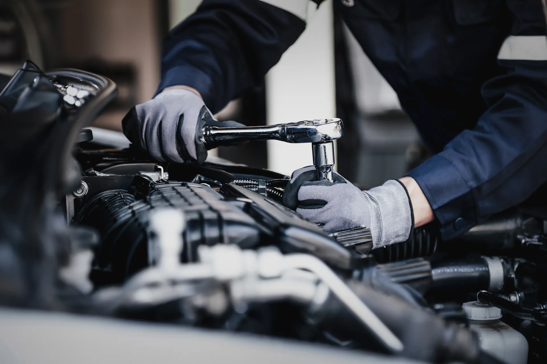 A Ridgepoint technician in work gloves and shop uniform working on an engine with a ratchet