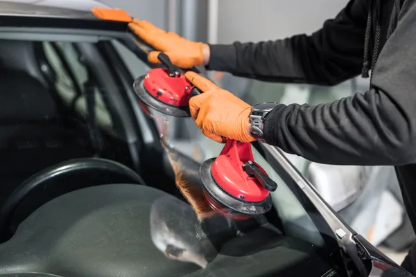 Auto glass technician fitting a replacement windshield to a vehicle in a service bay
