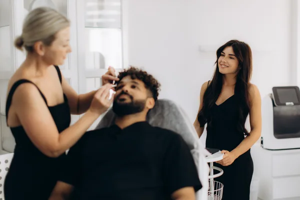 Permanent makeup artist microblading a client's eyebrows in a bright modern PMU studio