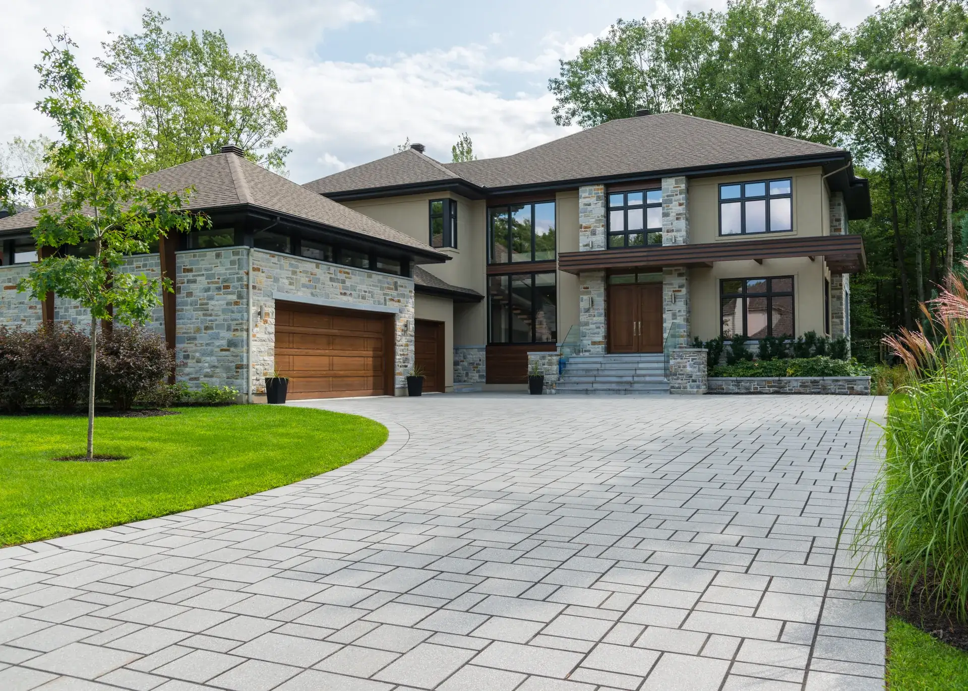 Briar Hollow Residence — a transitional stone-and-stucco custom home with a deep hip roof, quarter-sawn white-oak carriage doors and a granite paver arrival court framed by lawn and birches