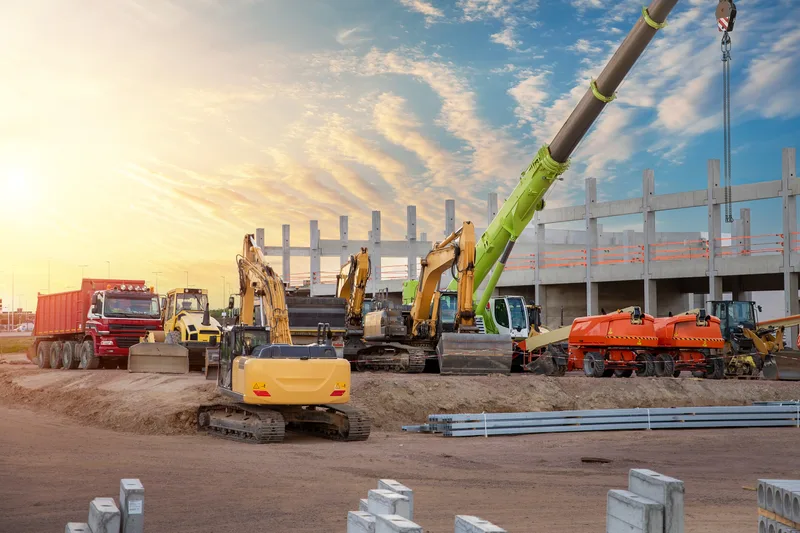 Construction equipment staged before a precast concrete structure at sunrise on an industrial site