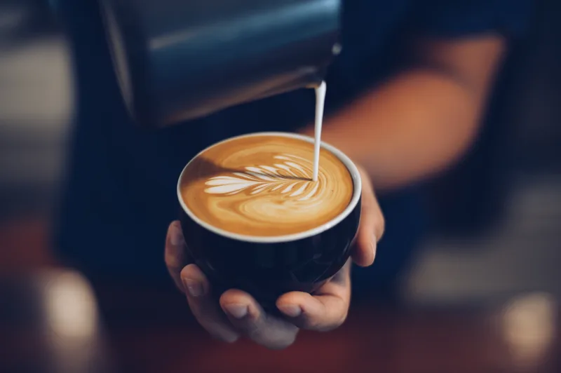 Barista pouring steamed milk into a cup of coffee, drawing latte art