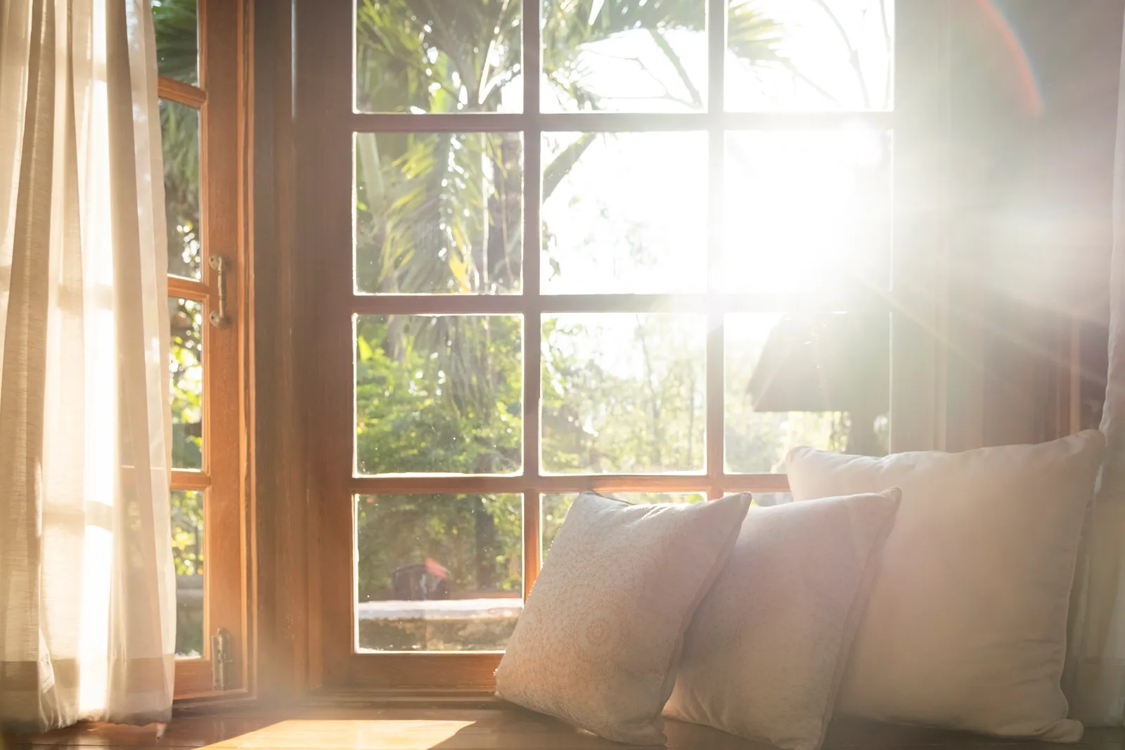 Morning sun pouring through a wood-framed window onto linen cushions on a window seat