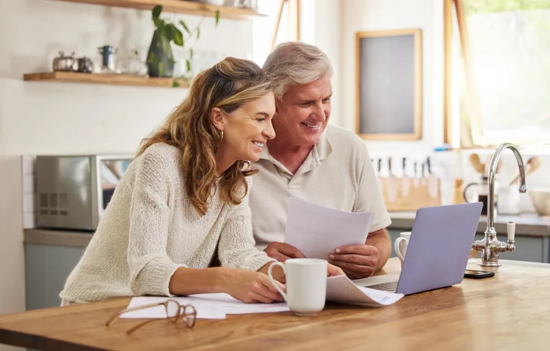 A couple at their kitchen table comparing a mortgage renewal letter against options on a laptop