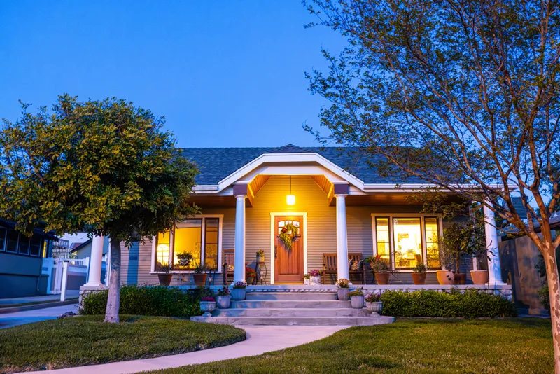 A craftsman bungalow at twilight, porch and windows glowing warm against a deep blue sky