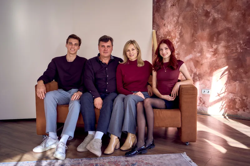 Two parents and their two adult kids sitting together on a couch at home, relaxed and smiling