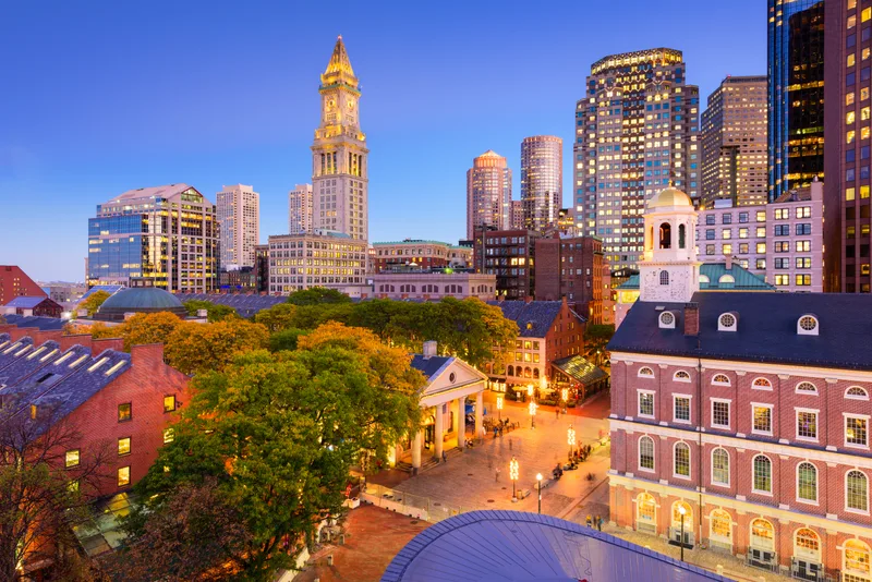 Boston's downtown skyline at dusk, with the historic Custom House tower rising over Quincy Market