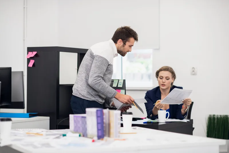 Two designers reviewing printed project documents in a bright studio