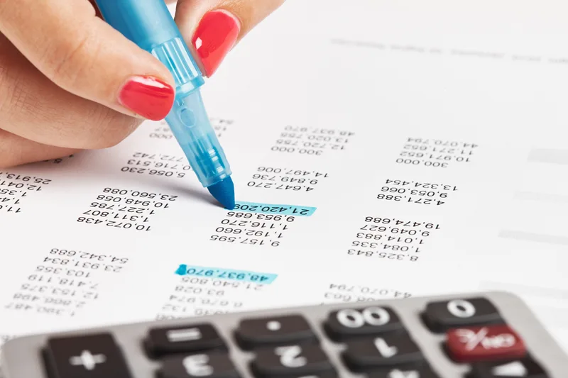 Close-up of a hand highlighting a figure on a printed financial statement beside a calculator