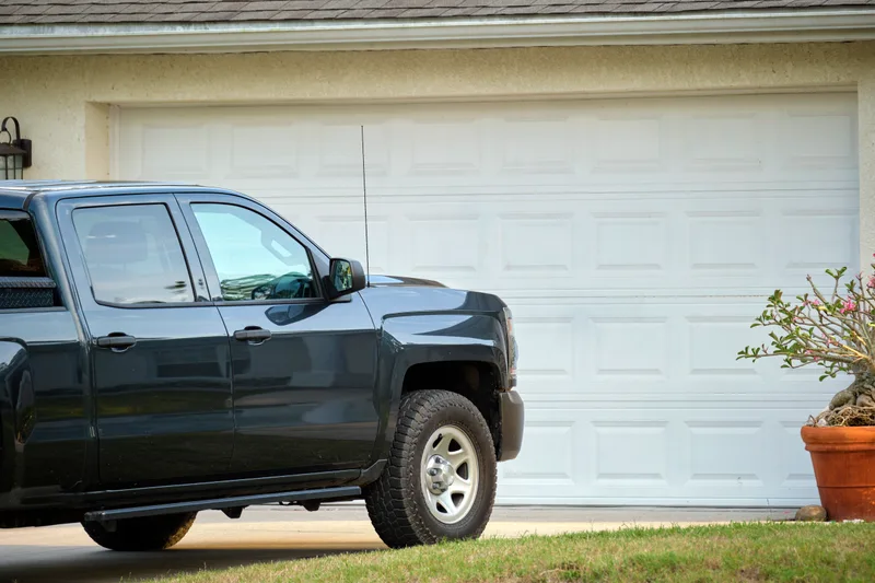A dark grey pickup truck parked on the driveway in front of a white double garage door on a suburban home