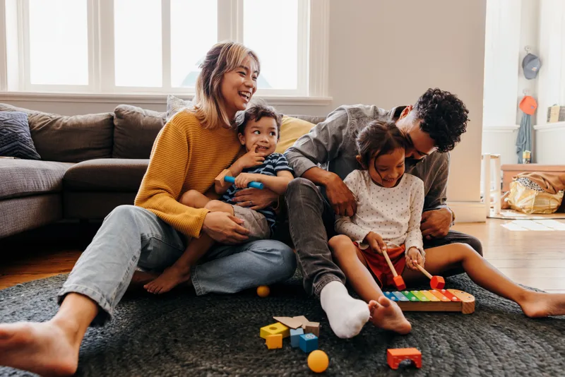 Young parents playing on the living-room floor with their two small children and a pile of wooden toys