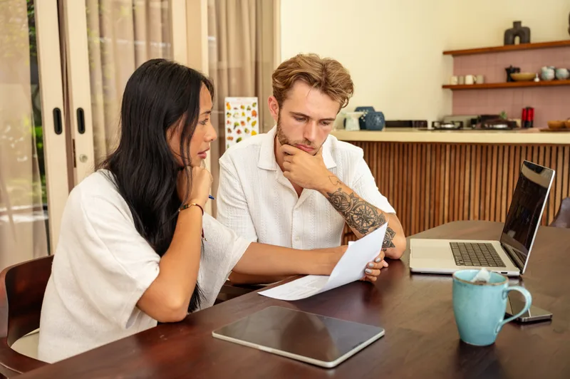 A couple at their dining table reading a financial document together beside a laptop