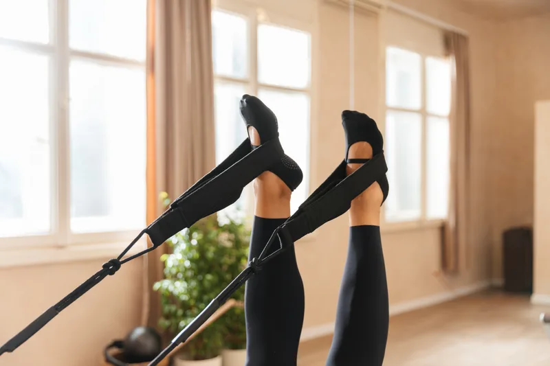 Student's legs in dark grip socks pressing overhead into reformer straps during a class