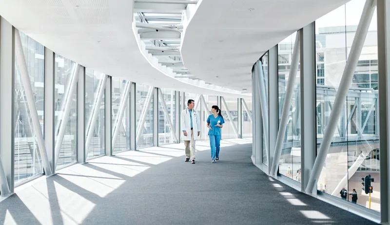 Physician and nurse walking through a bright glass skybridge connecting two Riverbank Medical Center buildings