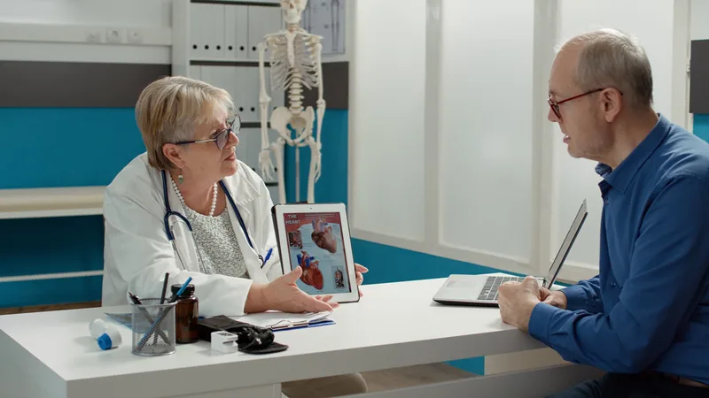 Cardiologist showing a heart anatomy diagram on a tablet to an older patient across a consultation desk