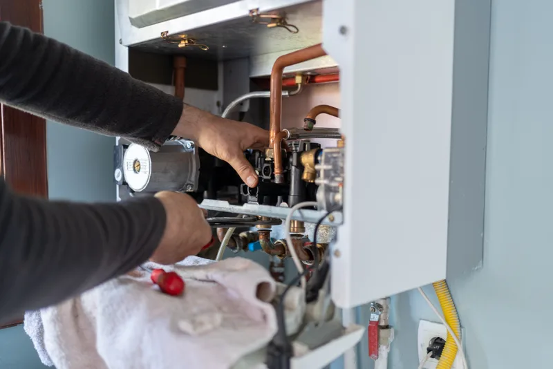 HVAC technician reaching into an open wall-hung heating unit to service its internal components