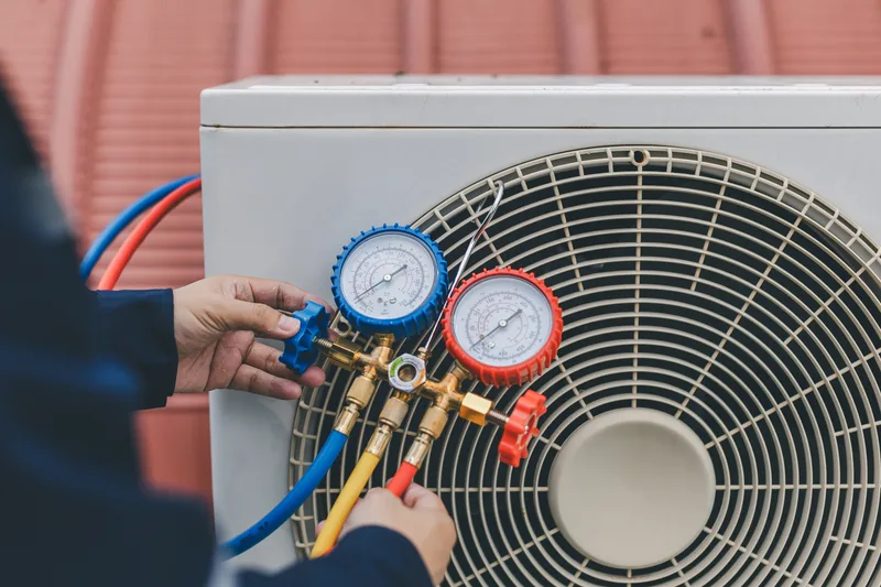 Technician reading refrigerant manifold gauges connected to an outdoor air-conditioning condenser