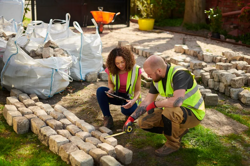 Two Verdant & Co. crew members in hi-vis vests measuring and laying reclaimed granite setts on site