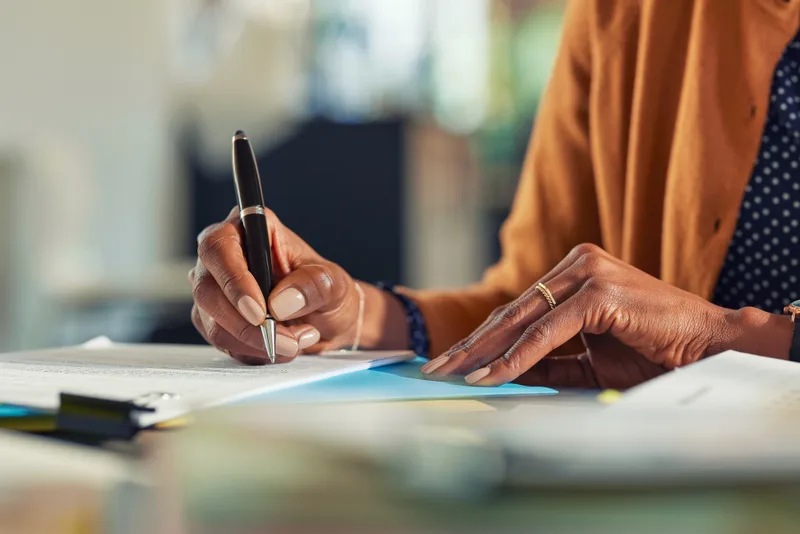 A close-up of a woman's hands signing an estate-planning document with a pen
