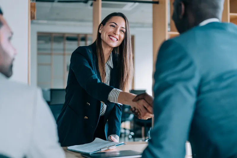 A broker shaking hands with clients across a meeting table after reviewing their mortgage paperwork
