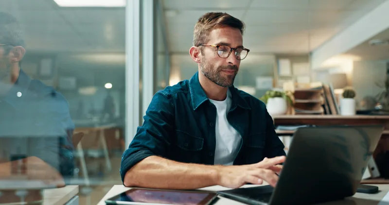A self-employed business owner working through paperwork on a laptop in his studio office