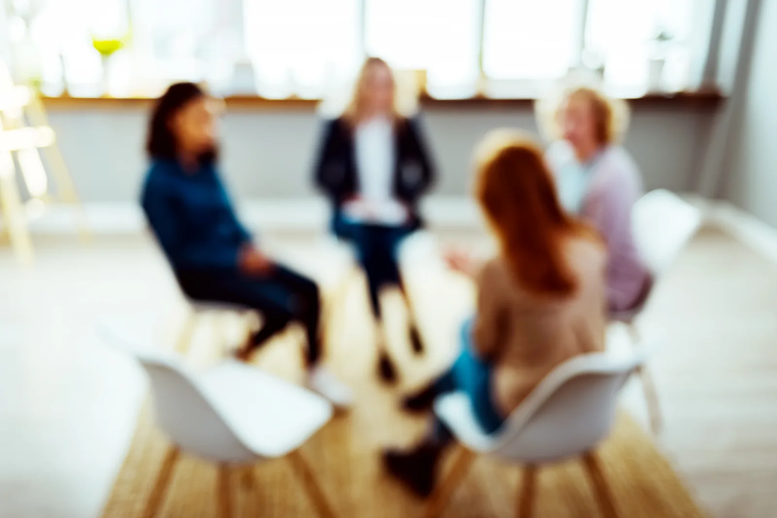 Counselor leading a supportive group therapy session in a sunlit room at an addiction treatment center