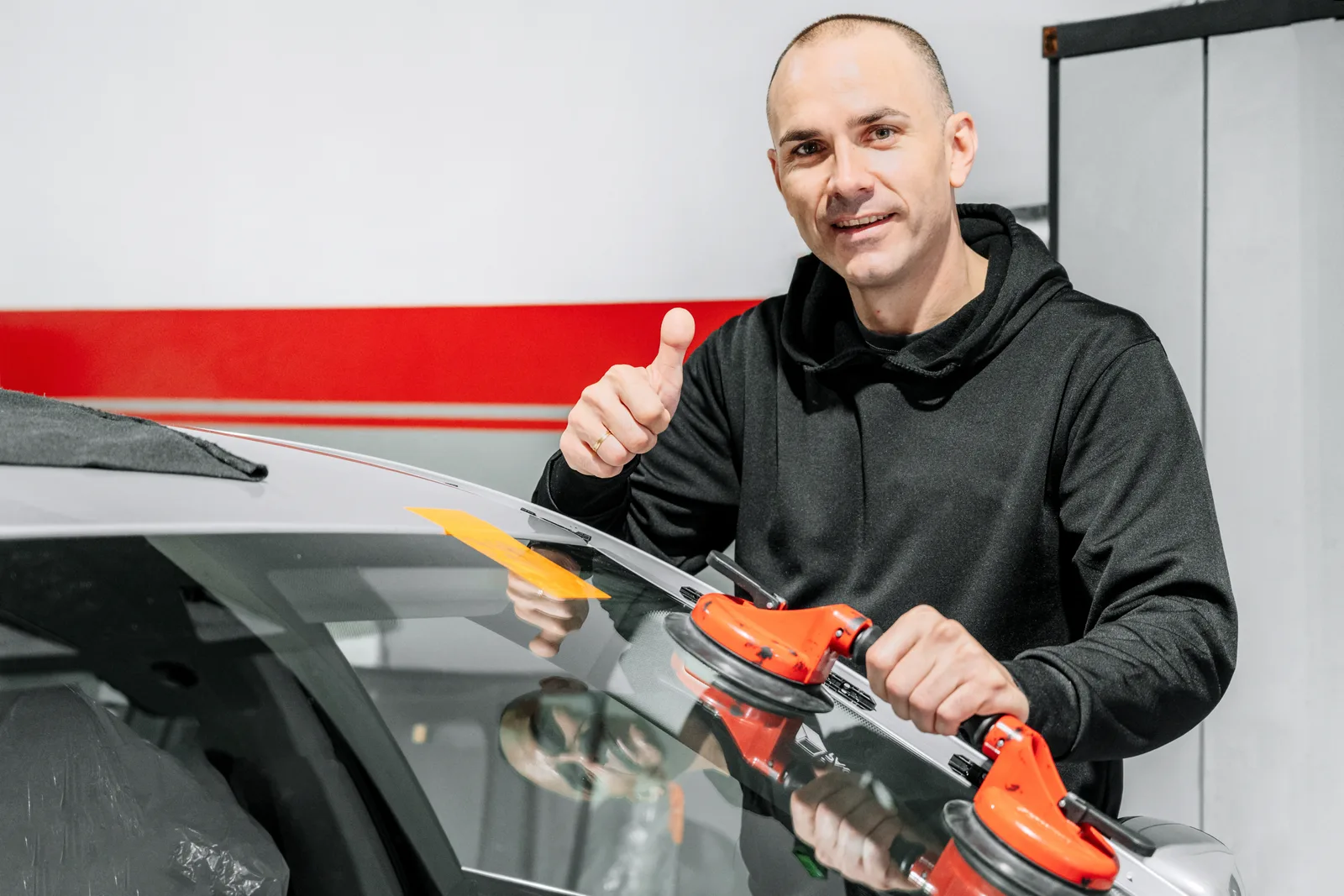 Auto glass technician fitting a replacement windshield onto a sedan in a customer's driveway