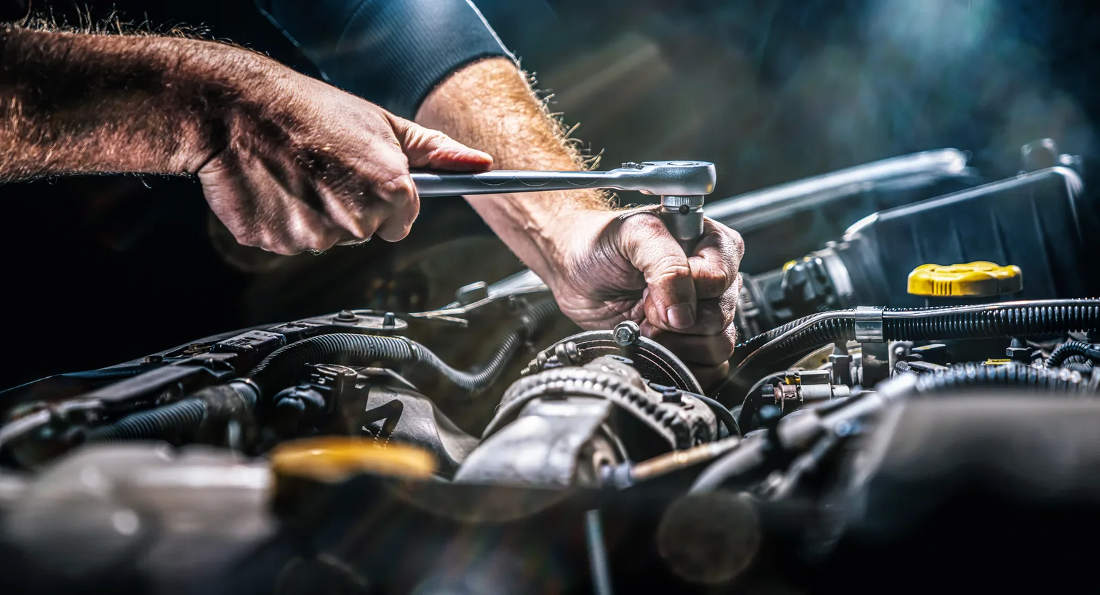 Mechanic's hands tightening an engine bolt with a ratchet in a repair shop service bay