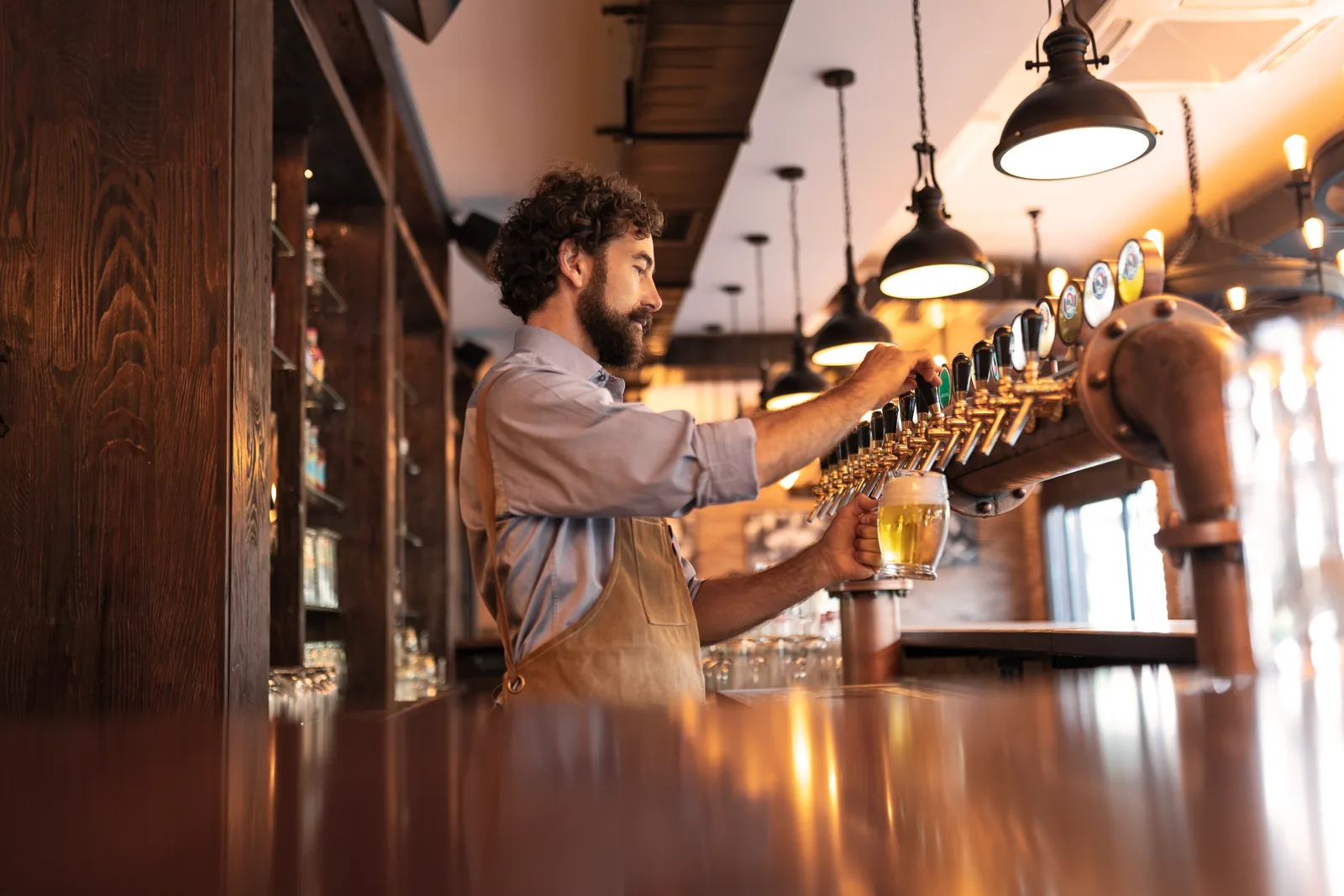 Bartender pulling a tap handle to pour a fresh pint behind the bar of a busy taproom