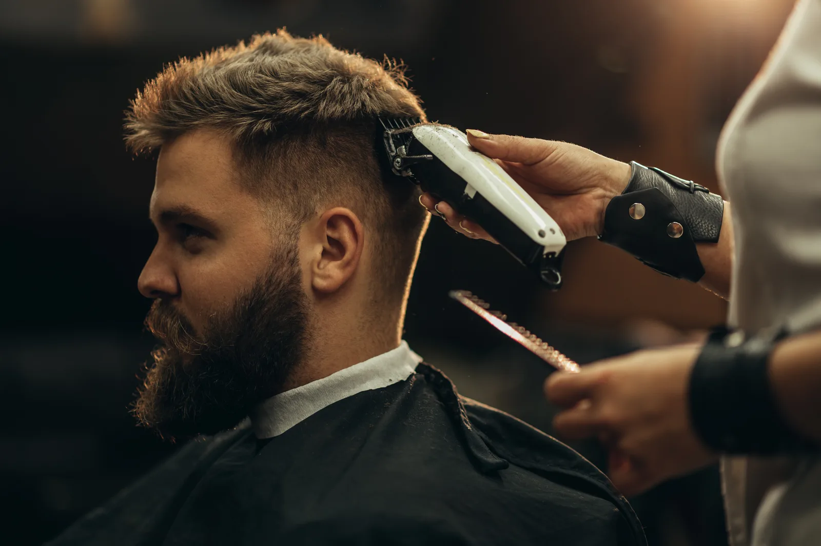 Barber shaping a client's fade with clippers in a busy barbershop