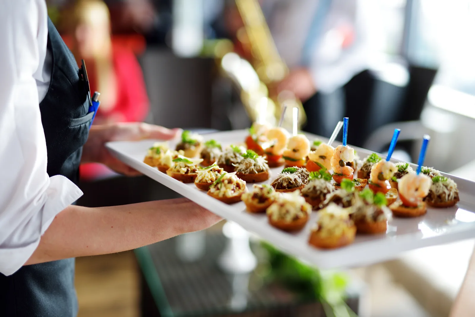 Catering server carrying a tray of garnished canapés to guests at a reception