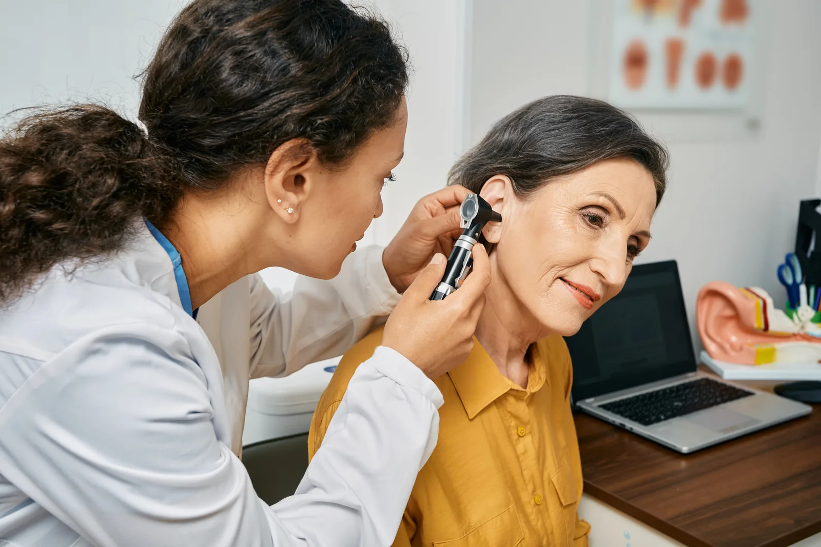 ENT specialist checking a seated patient's ear canal with an otoscope in an exam room
