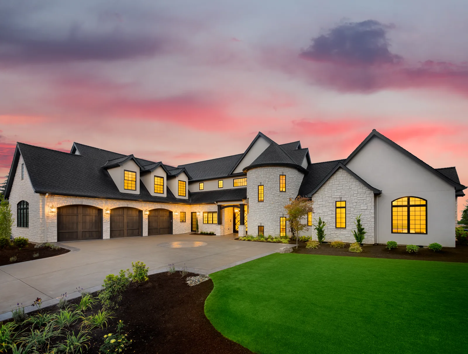 Custom-built two-story home at dusk with warm interior lighting and a landscaped front yard