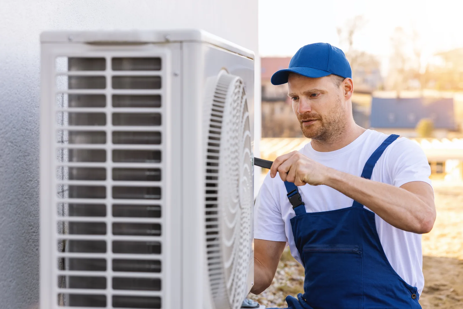 HVAC technician checking a backyard air-conditioning condenser during a summer service call