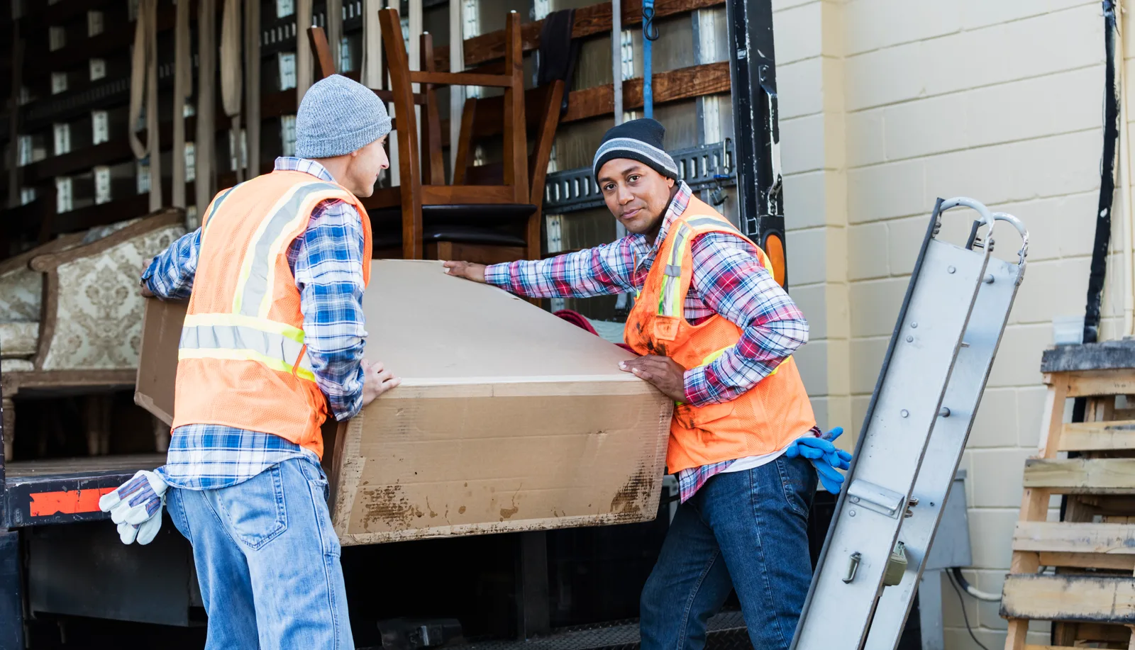 Junk removal crew carrying an old couch up the ramp of their box truck outside a customer's garage