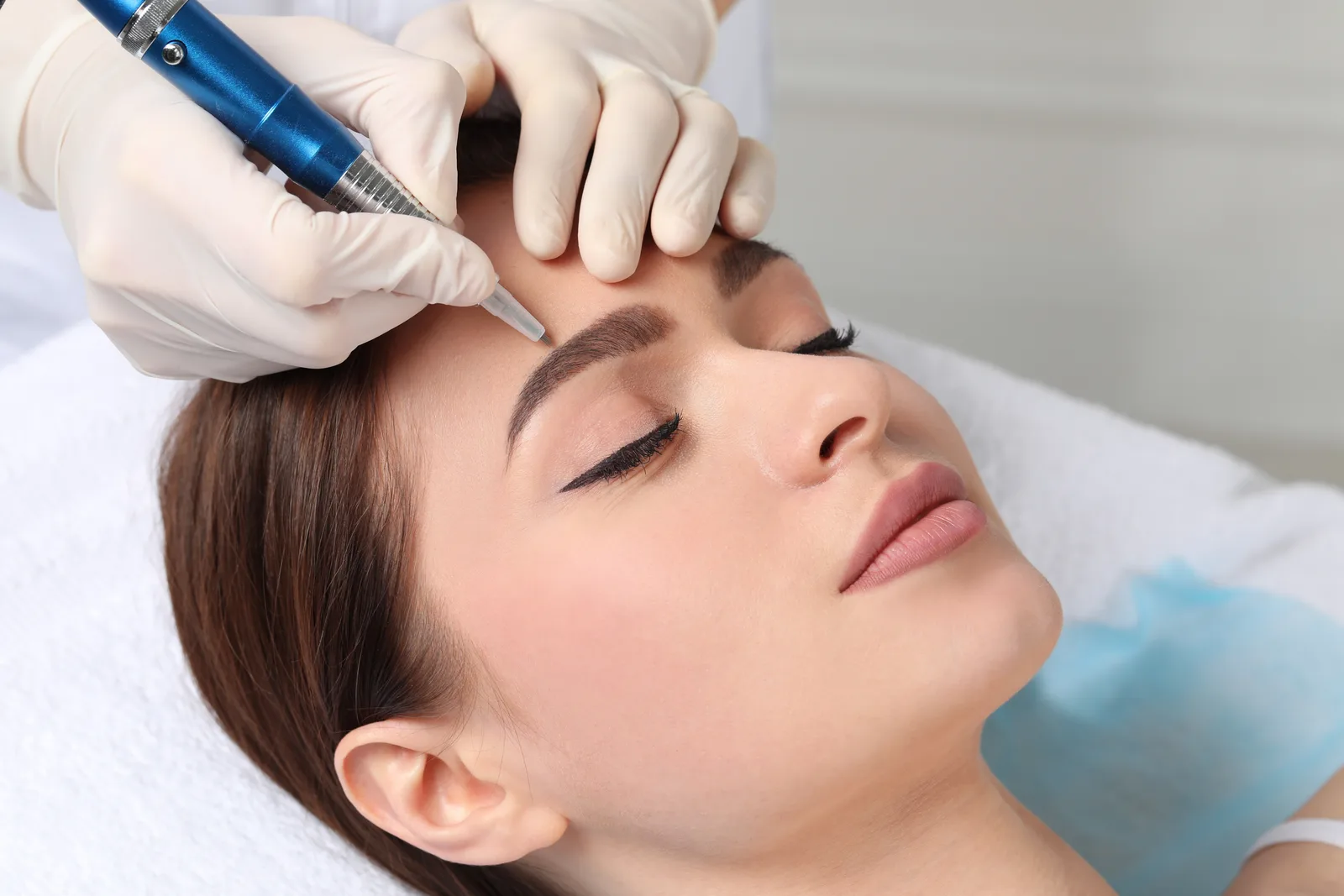 PMU artist etching fine hair strokes into a client's eyebrow with a microblading hand tool at her studio
