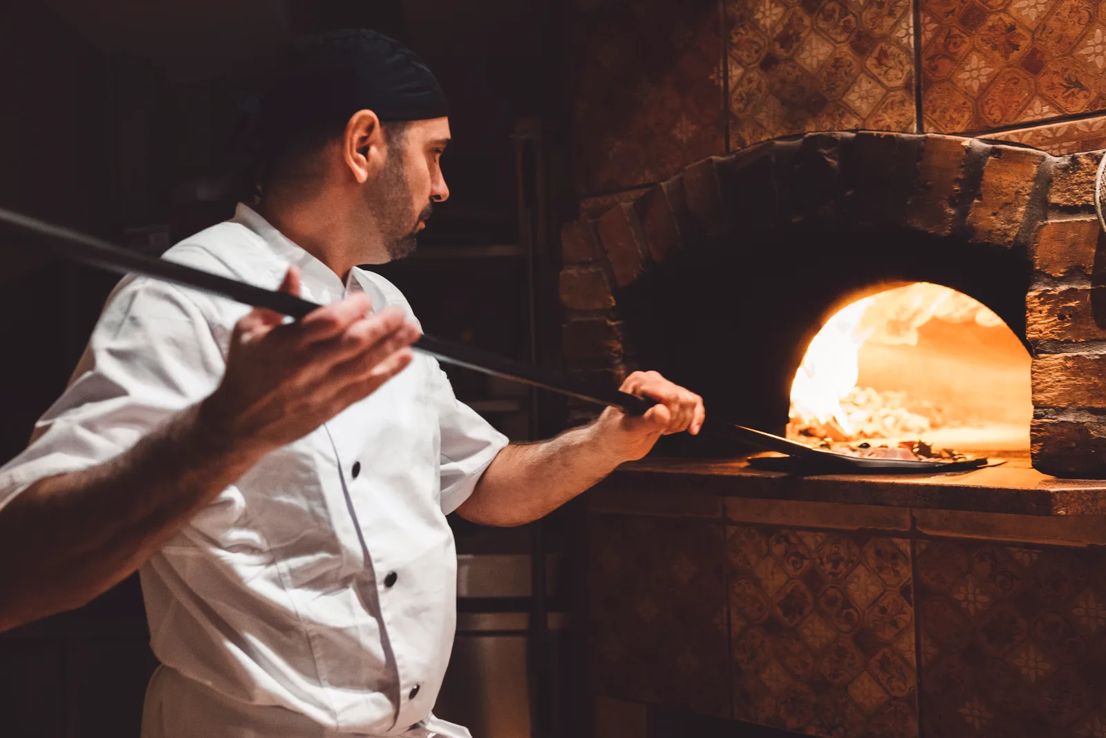Pizza maker sliding a fresh pie into a wood-fired oven during the dinner rush