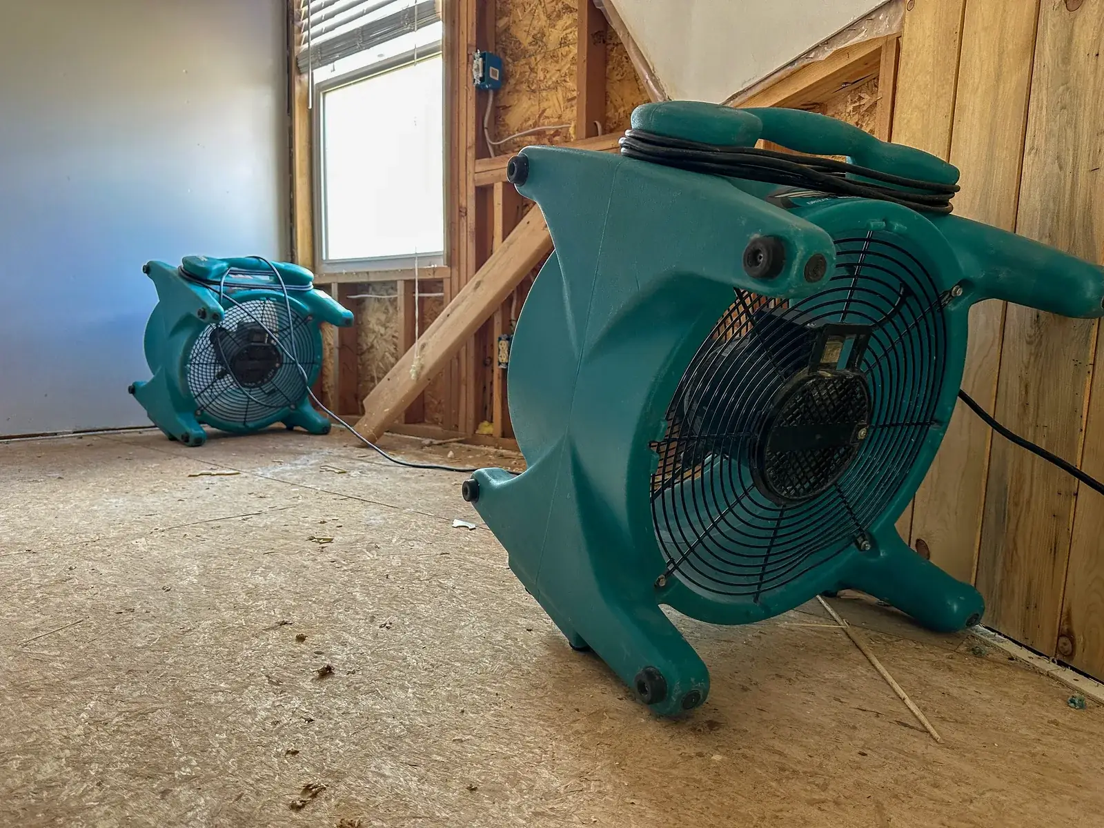 Restoration crew's air movers drying a flooded family room stripped to the studs and bare subfloor